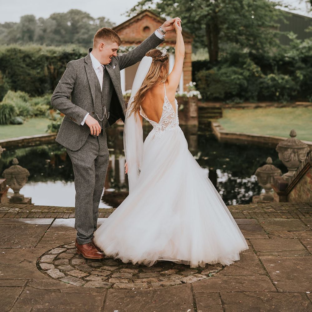 Groom in grey tweed suit spins around bride in tulle skirt at country house rustic wedding venue