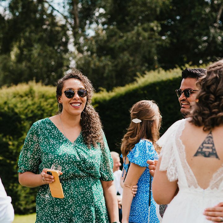 Wedding guests enjoy themselves in the sunshine wearing sunglasses and drinking