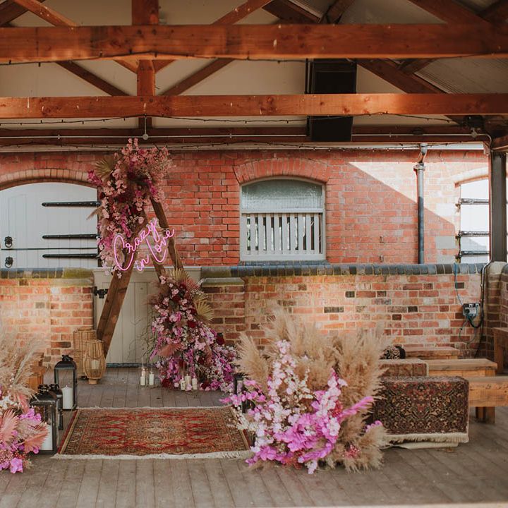 Aisle and altar style at Prestwold Hall Barns wedding venue in Leicestershire with wool rugs, dried grasses, pink cherry blossom, lanterns and a wooden triangle frame. 