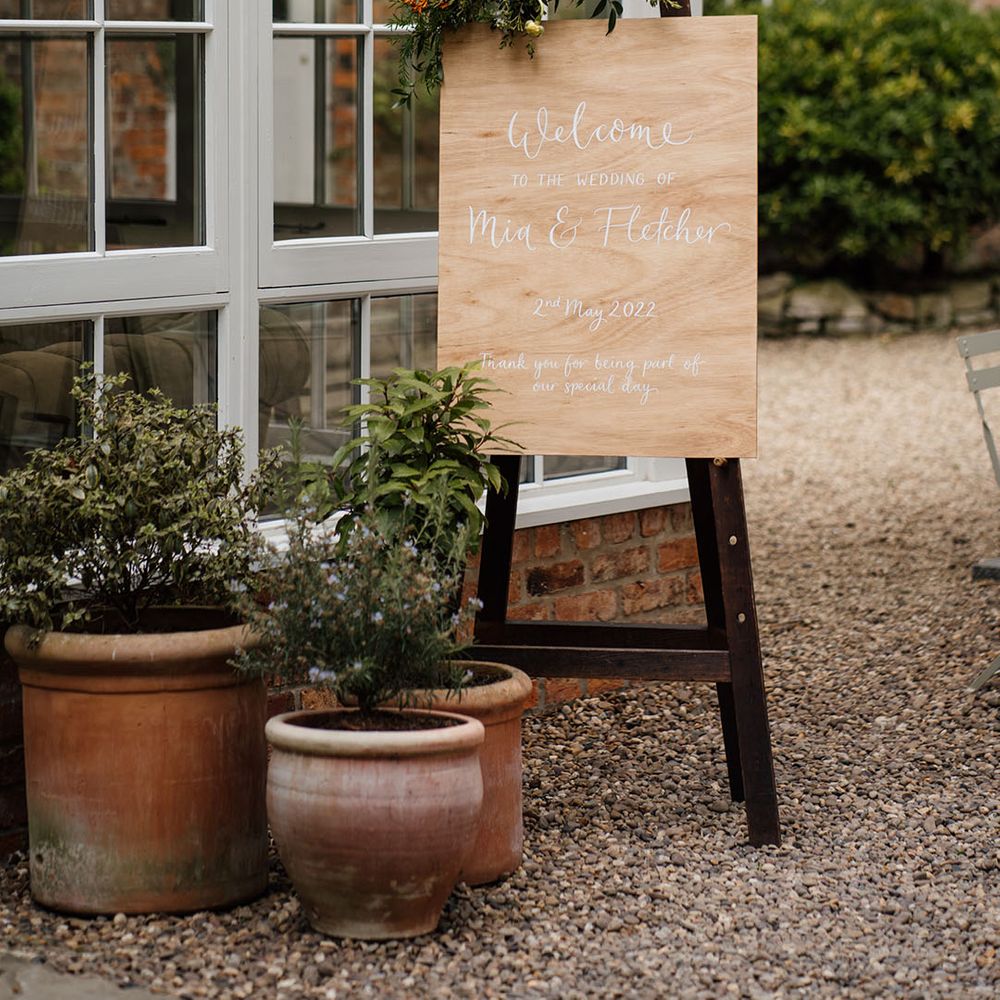 Wooden welcome wedding sign with white font decorated with flowers and greenery 