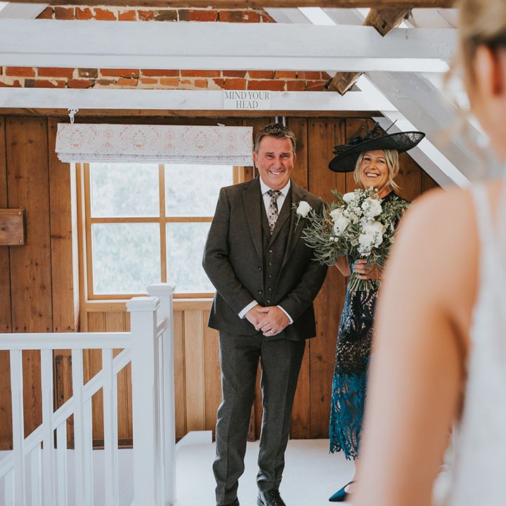 Parents of the bride smile as they get the first look at her in her wedding dress 