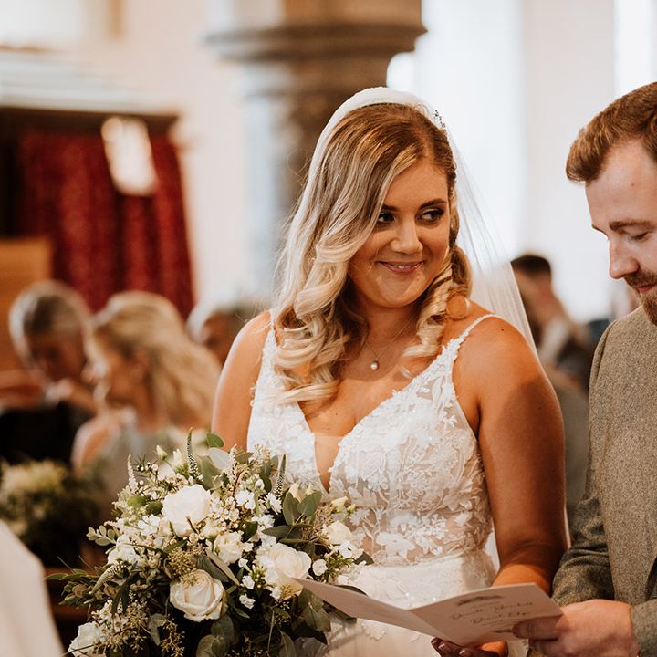 The groom looks at the order of service booklet while the bride smiles at him adoringly during their church ceremony 