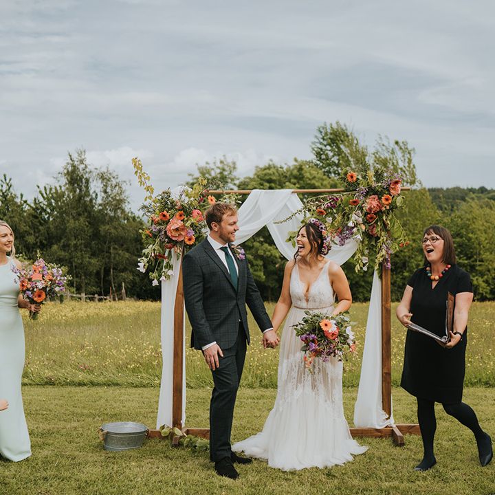 Bride & groom during outdoor wedding ceremony complete with wooden arch and colourful floral decor with drapes 