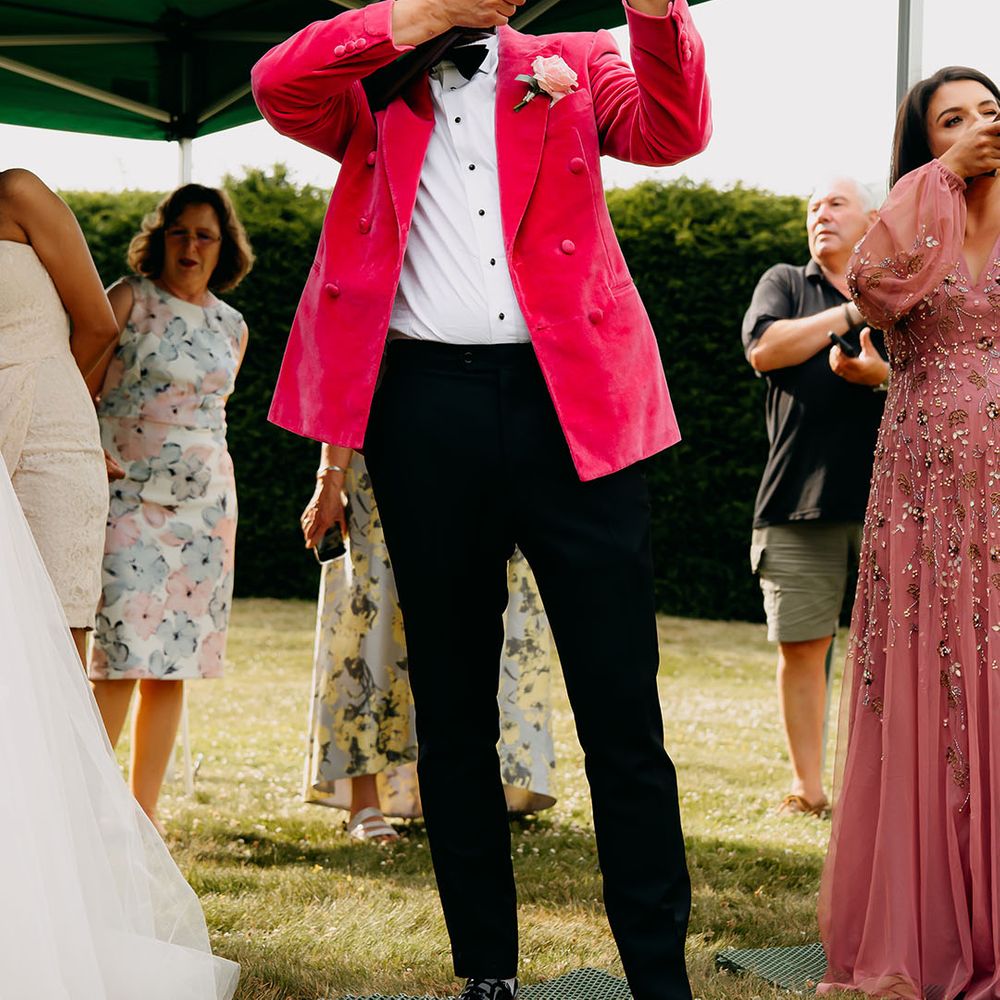 Groom in pink velvet suit jacket with a gun to play laser shooting for the wedding entertainment 