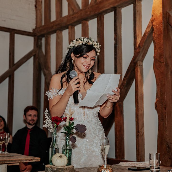 The bride stands holding a microphone and paper of her speech as she gets emotional reading it out 