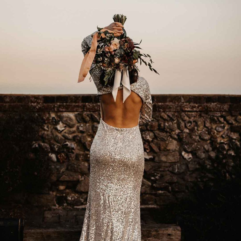 Bride in silver sparkly wedding dress with open back detail holding bridal bouquet behind her head 