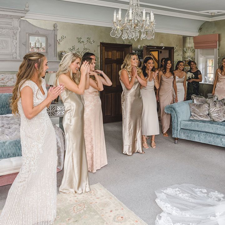Bridesmaids in mismatched gold bridesmaid dresses for the wedding all looking at the bride for the first time 