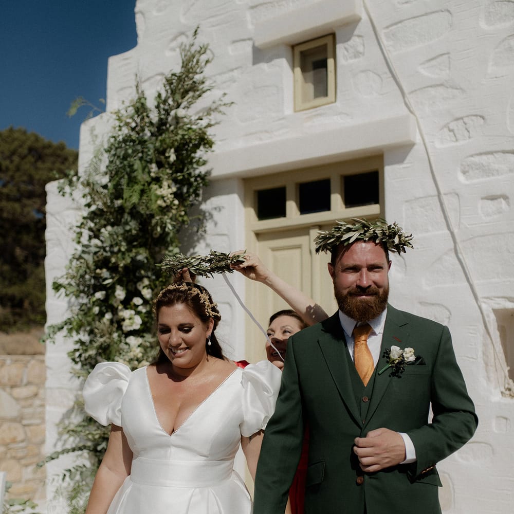 Bride and Groom taking part in the Greek wedding tradition of Stefana crowns during intimate ceremony at white chapel