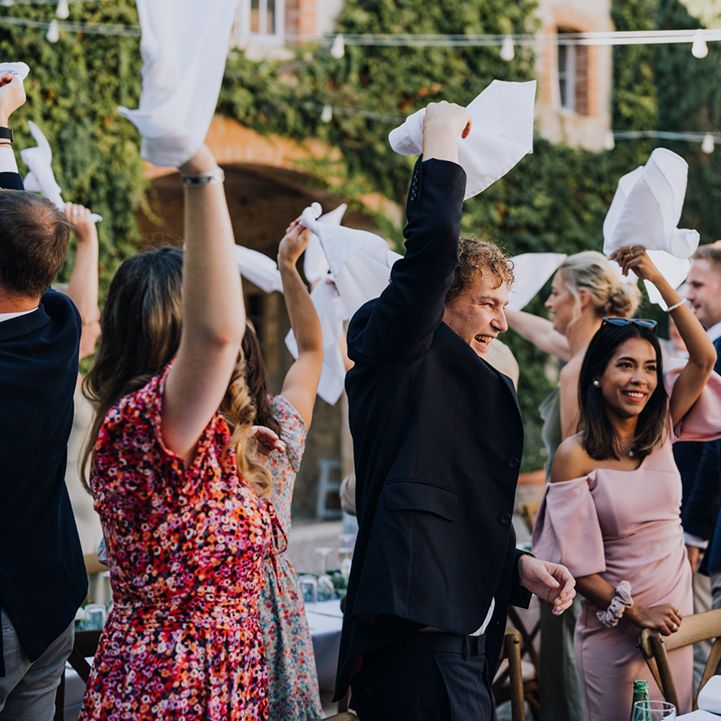 wedding guests waving napkins in the air at an outdoor destination wedding reception 