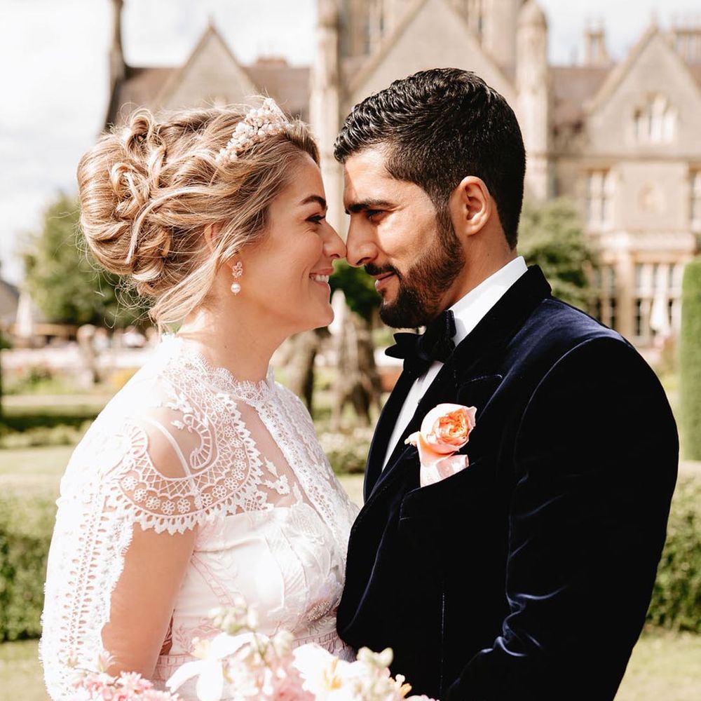 Bride holding pink and white oversized wedding bouquet in long sleeve lace wedding dress with the groom in blue velvet tuxedo 
