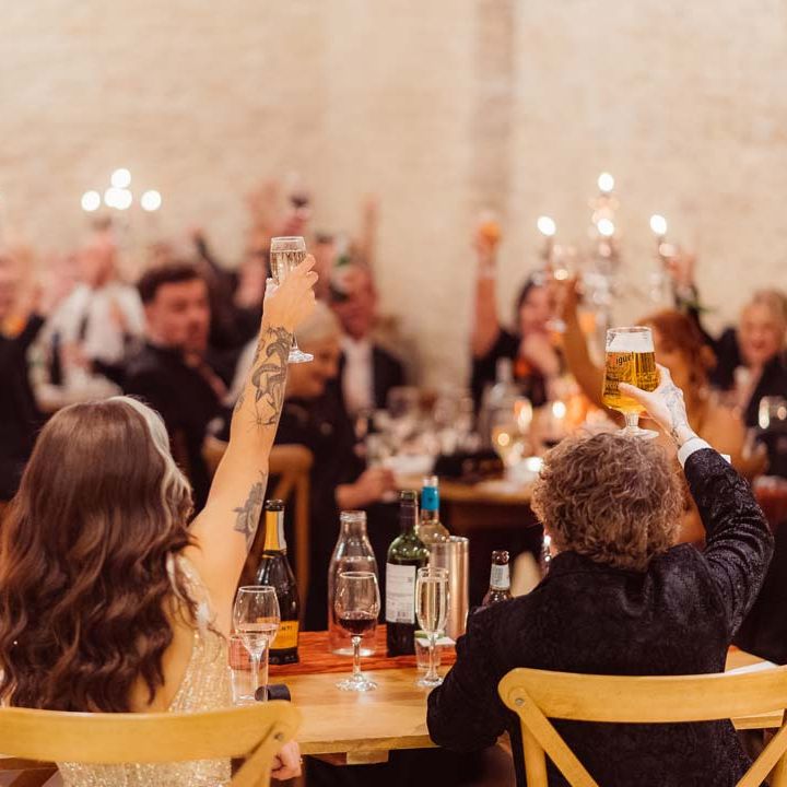 Bride and groom raising a glass to wedding guests during wedding speeches at Kingscote Barn Tetbury wedding venue 
