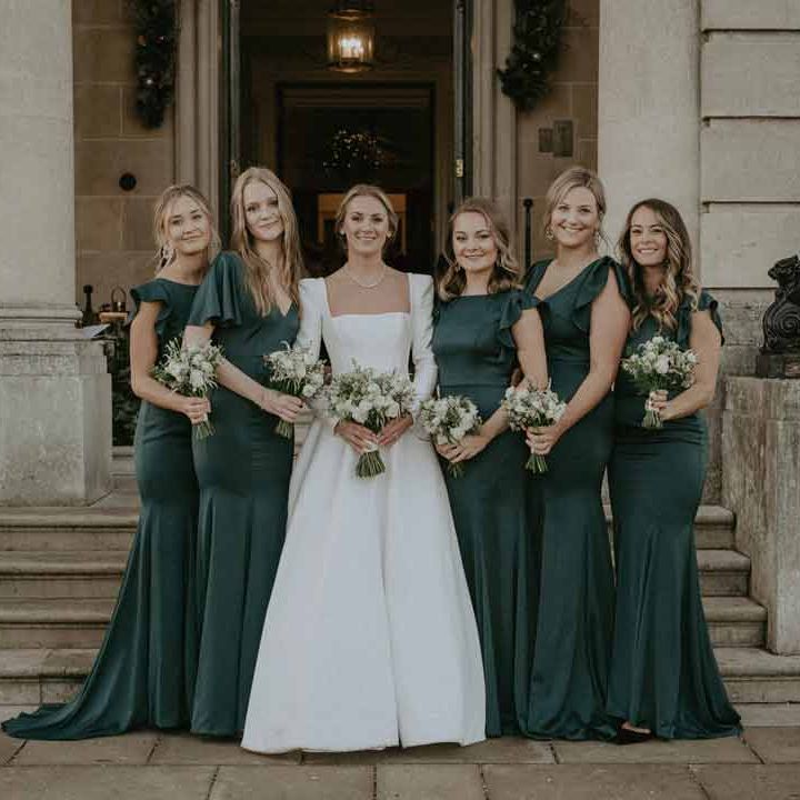 Bride in classic square neck long sleeve wedding dress standing with bridesmaids in bottle green mismatched bridesmaid dresses at Hedsor House