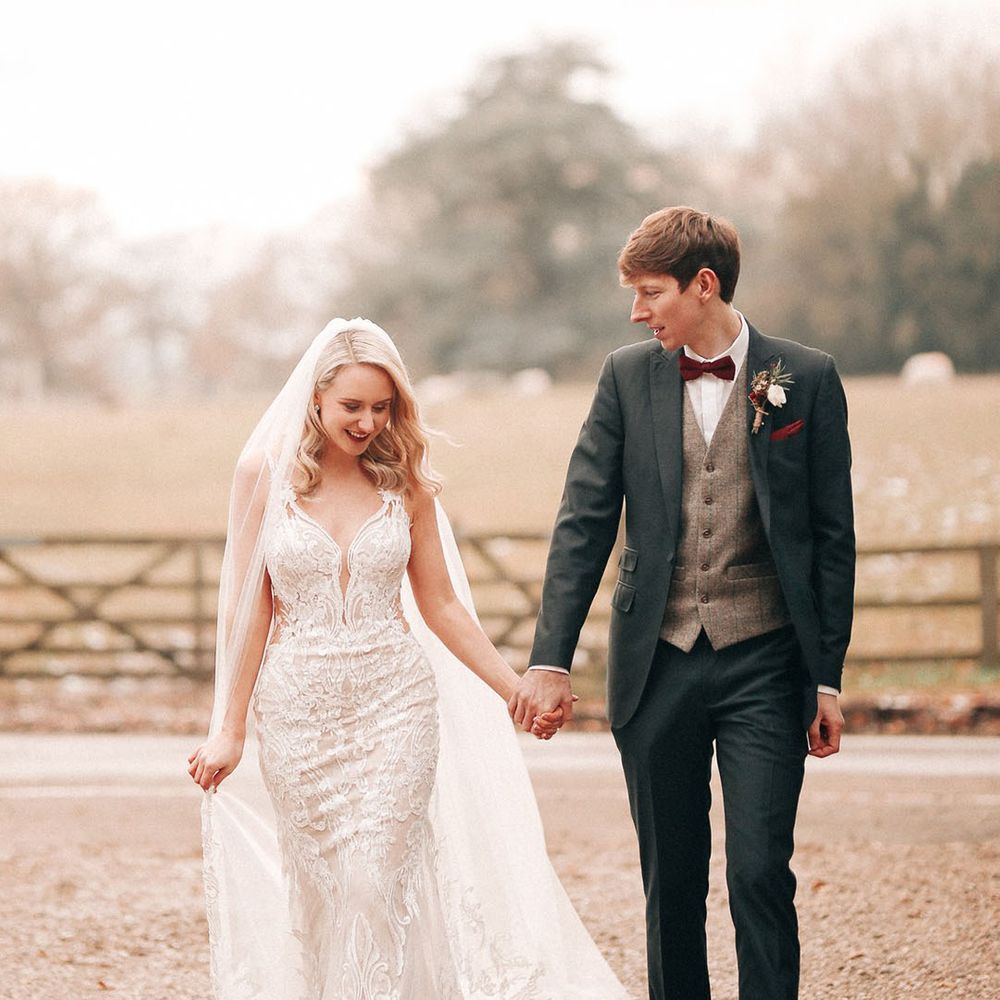 Groom in navy three piece and red bow tie with bride in embellished lace wedding dress 
