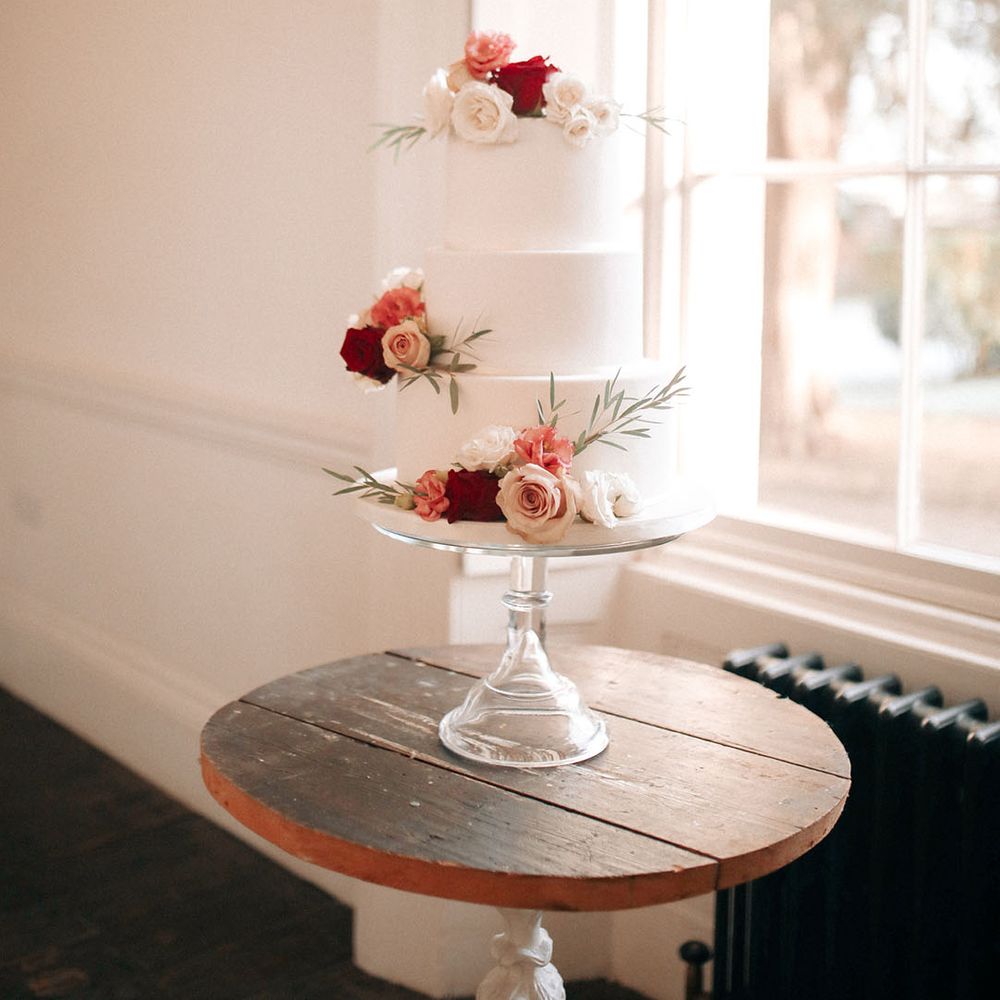 Three tier white iced wedding cake decorated with red, pink, and white rose decor 
