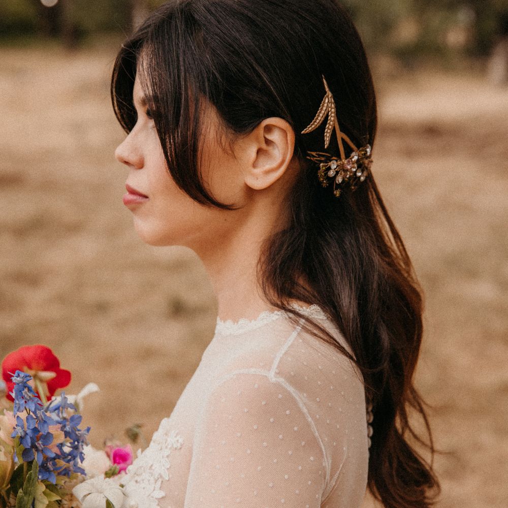 Bride wears her dark hair pulled back into a low updo complete with golden accessories  