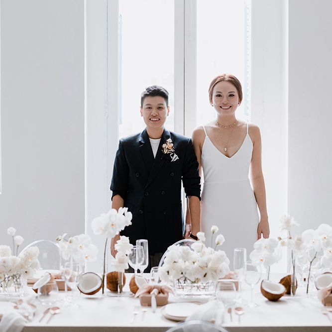 Two brides standing at their intimate reception with all white minimalist wedding decor 