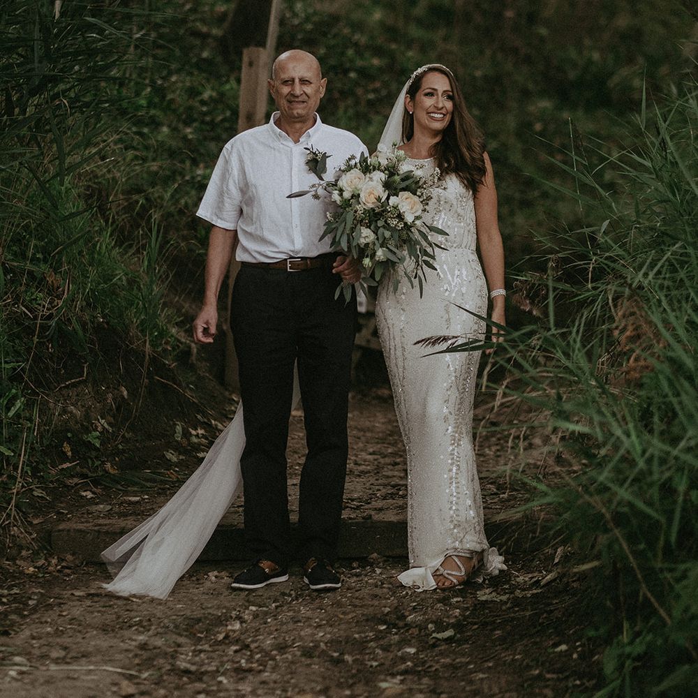 Bride walks with her father on wedding day through greenery 