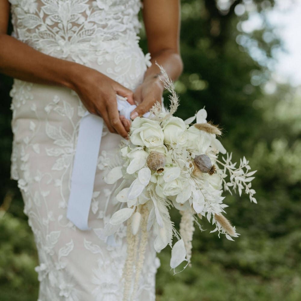 Boho bride holding bouquet of dried poppy heads, white roses, white flowers and white leaves