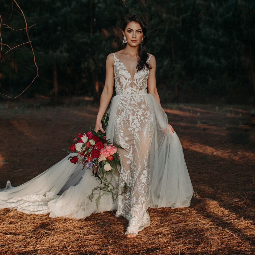 Bride with long brown side swept hair in the woods in a fitted lace wedding dress with plunging neckline and detachable chiffon skirt 