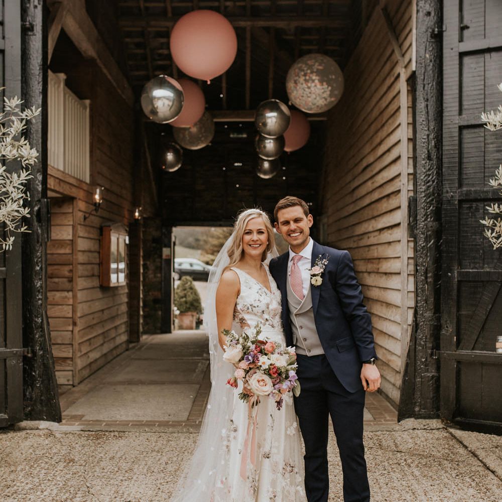 Spring Prezola wedding couple in a floral embroidered wedding dress and navy suit standing in the courtyard of their wedding venue 
