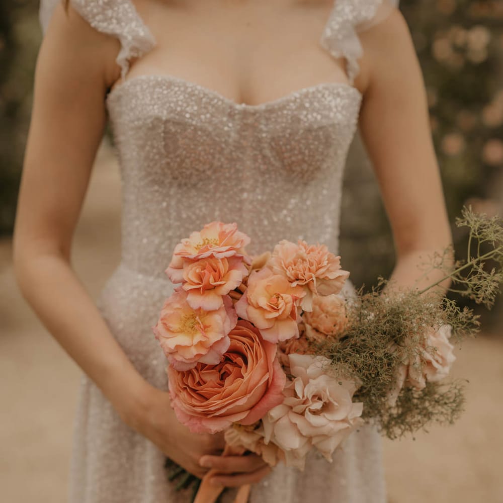 Bride in a sparkly Made With Love dress holding an orange, coral and peach wedding bouquet 
