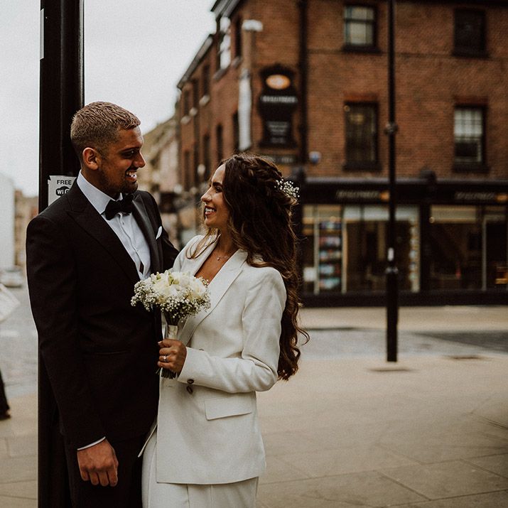 Groom in black tuxedo from Reiss smiling at his bride in a white suit at their Sheffield Registry Office wedding 