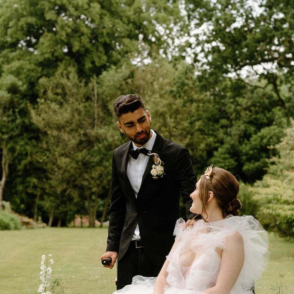 Portrait of the groom in a tuxedo looking at his bride in a tulle wedding dress as she sits in her wheelchair 