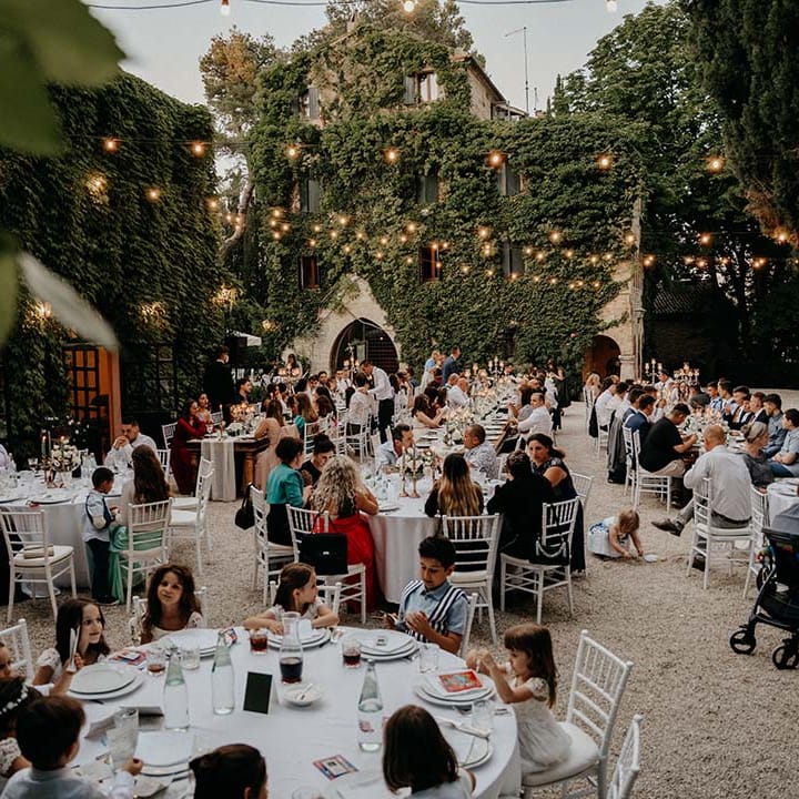 Wedding guests sit outdoors during wedding reception surrounded by villa  | Royal Studio