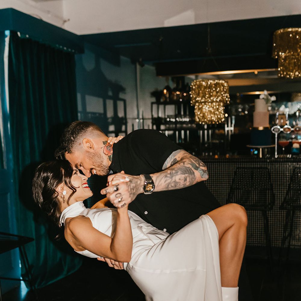 Groom with tattoos in a short sleeve black shirt leaning his bride over on the dance floor revealing her white boots 