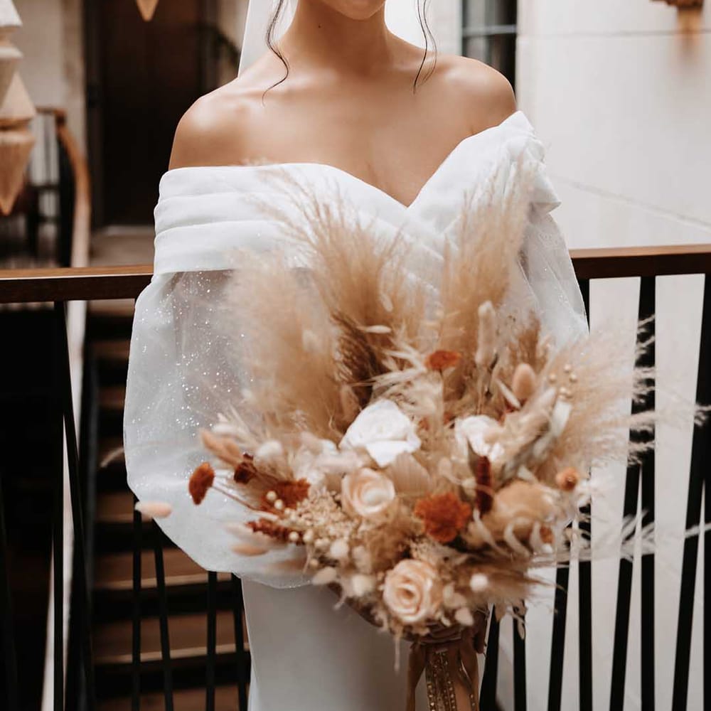 Sparkles in chiffon puff sleeves in brides wedding dress holding a autumnal colour palette bouquet 