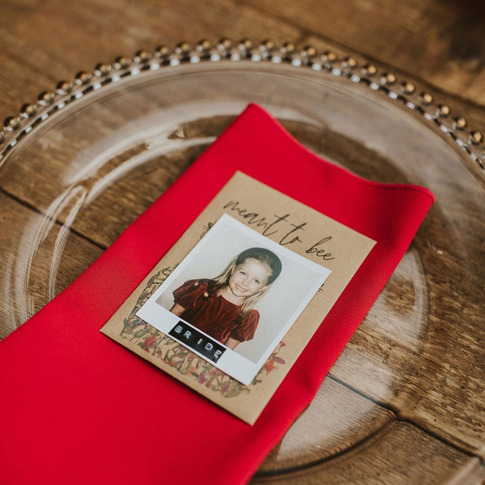 Place setting glass charger plate, red napkin and polaroid picture name place card 