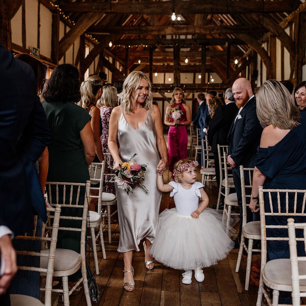Flower girl in a tulle skirt, trainers and flower crown walking down the aisle 