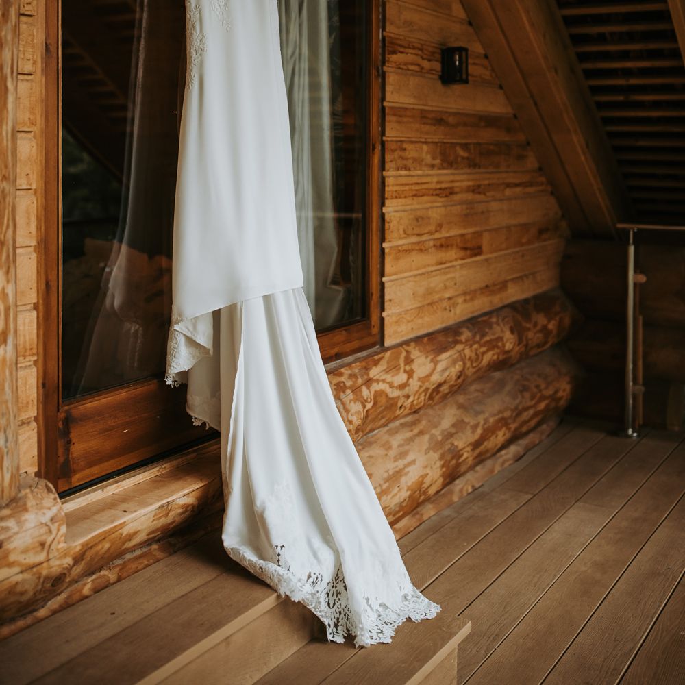 Lace wedding dress with train hanging in barn for rustic Lake District wedding