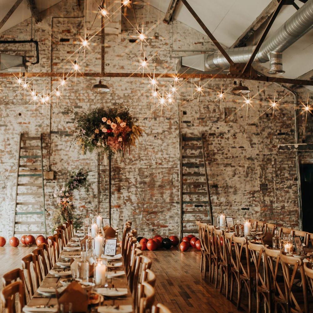 Interior of wedding reception room at Scale wedding venue in Liverpool with exposed brick, long wooden wedding table, flower cloud and bulb string lights
