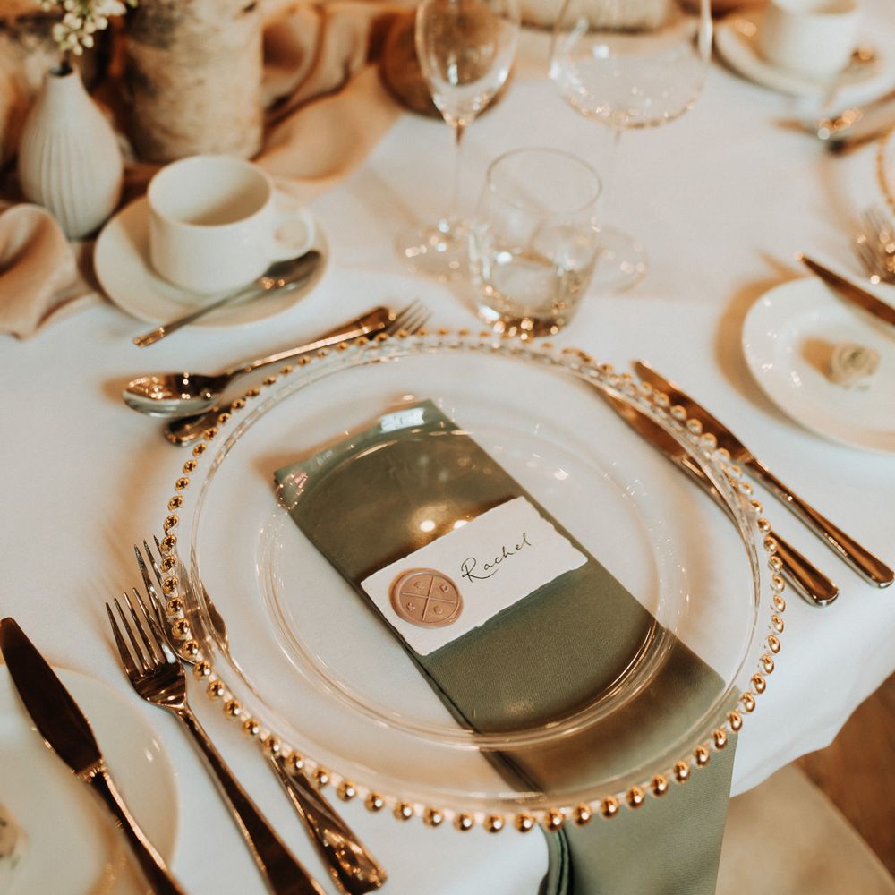 Clear plate with gold trim, caligraphy table place names and green napkins for chic wedding table setting