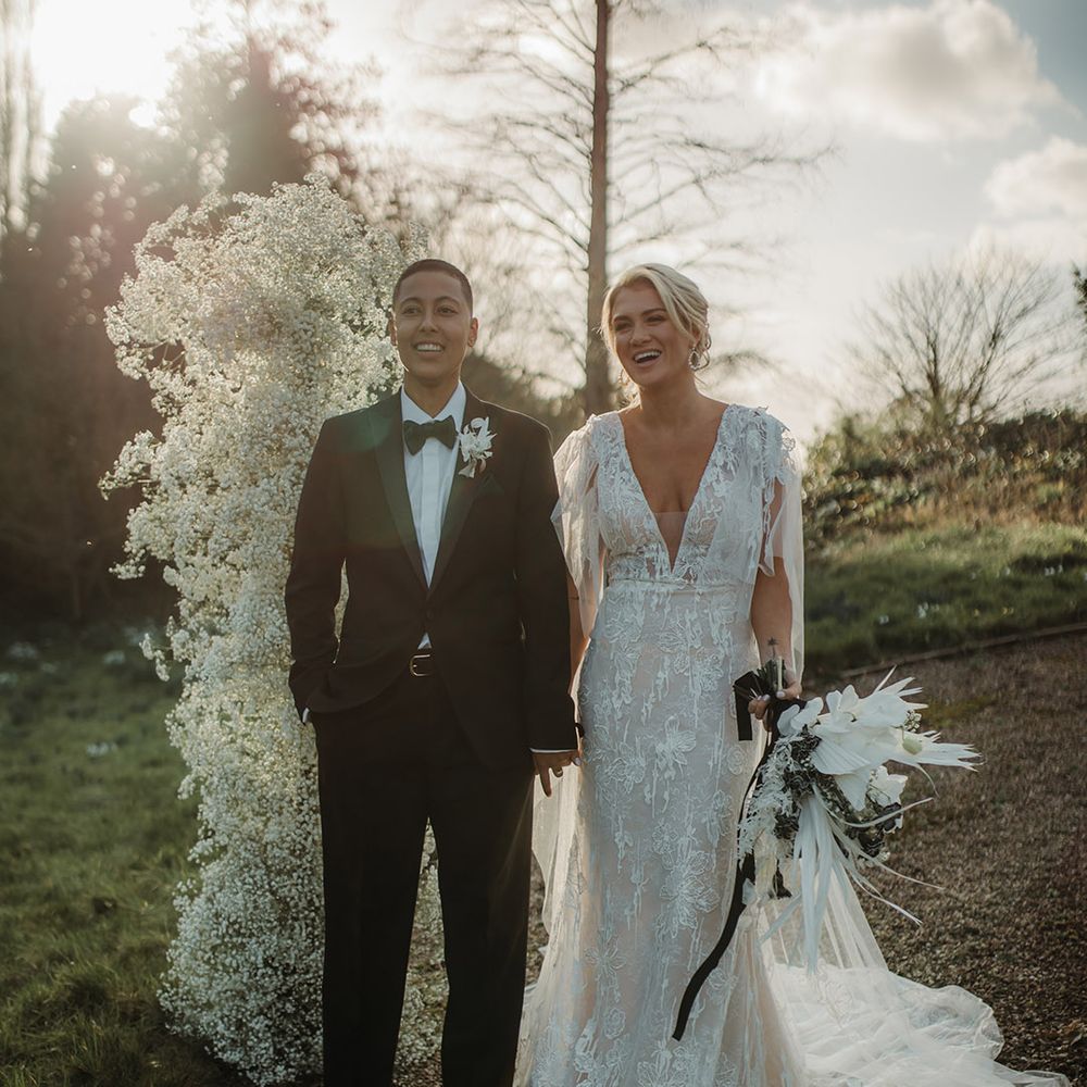Golden hour wedding photograph of an LGBTQI+ couple holding hands at Hodsock Priory wedding in a black tie suit and lace wedding dress