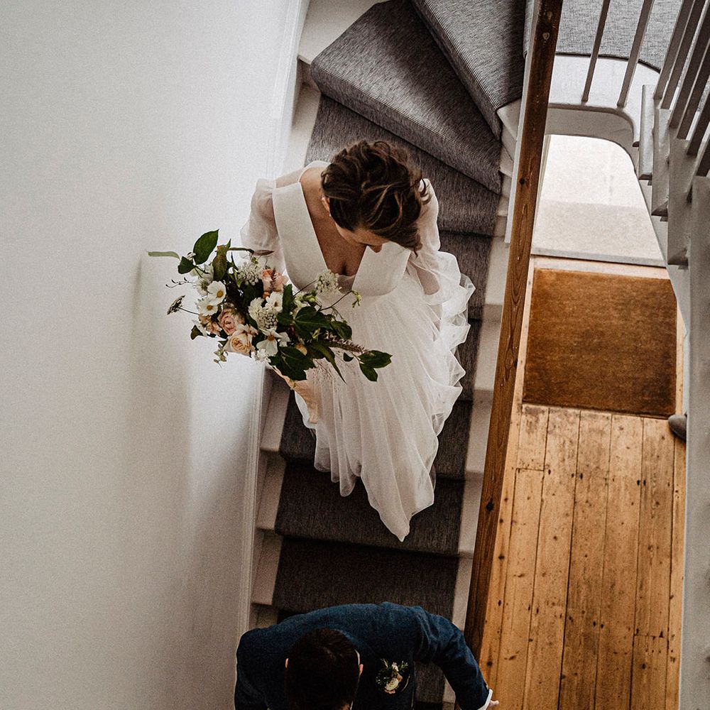 Bride carrying pink rose and dahlia bouquet with white cosmos flowers as she descends the stairs with the groom