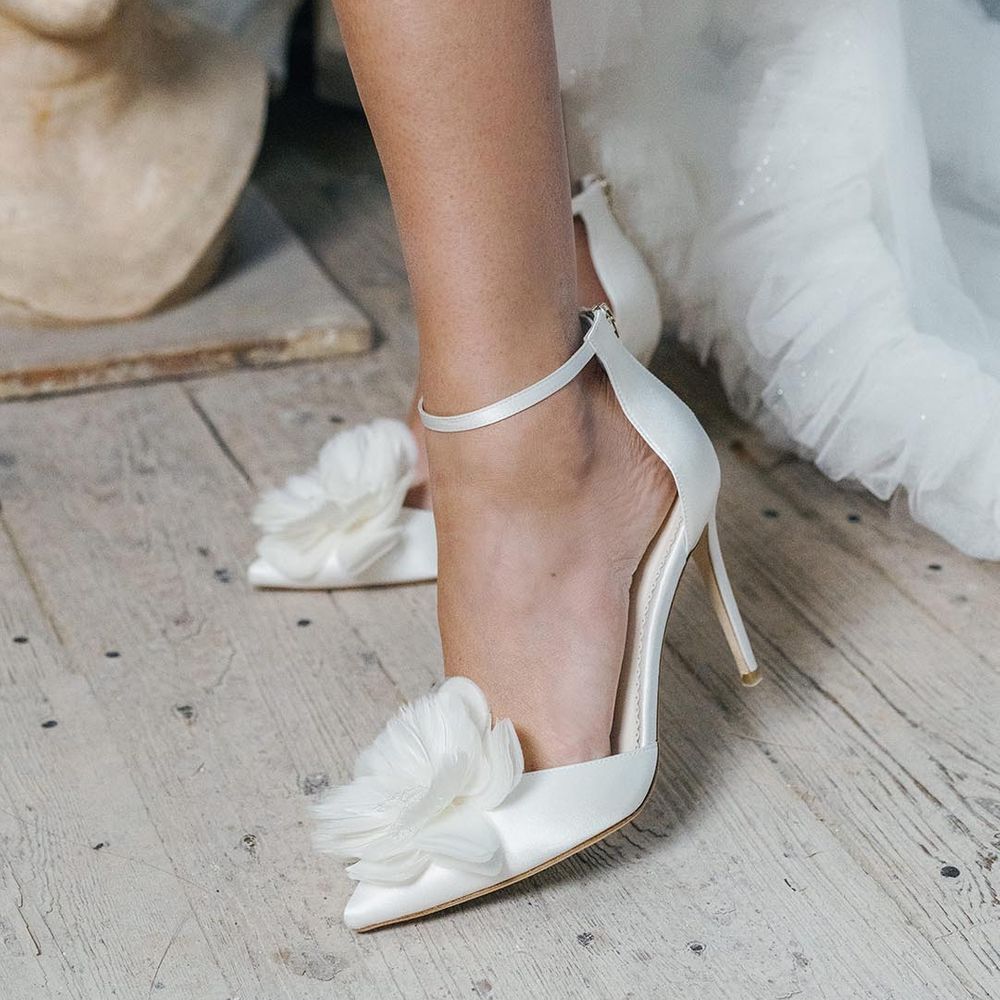 White stiletto wedding shoes with white flower and ankle strap worn by bride with ruffle wedding dress 