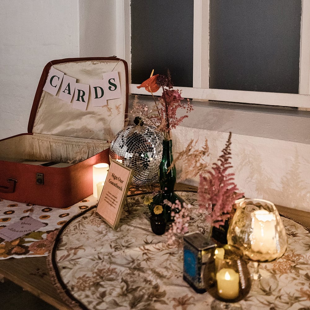 Open suitcase for wedding cards and guestbook with vases of flowers and candles with disco ball and sign in gold photo frame