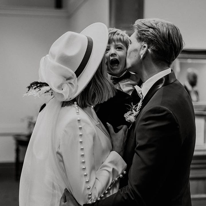Bride and groom kiss little boy on either cheek in black tie for town hall wedding 