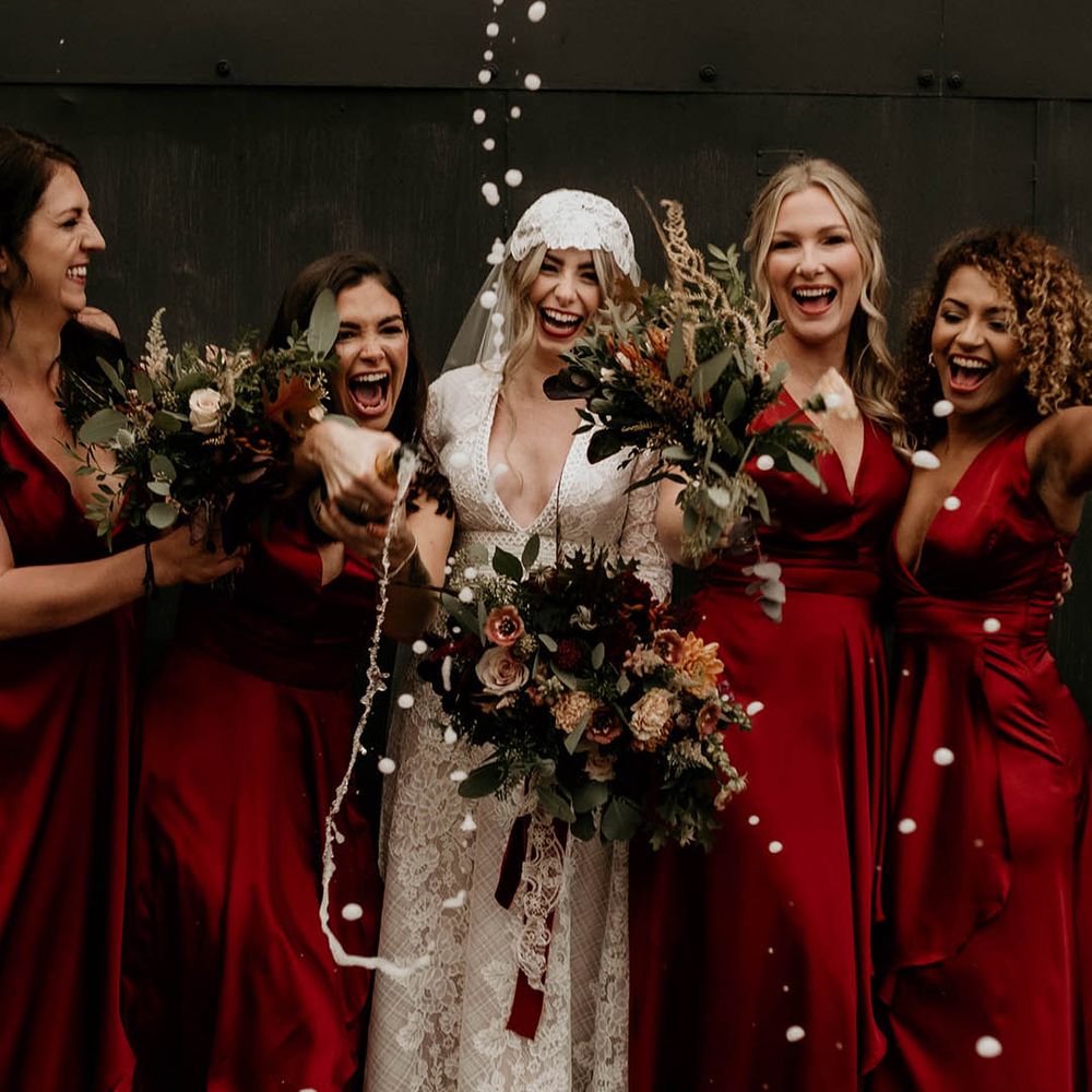 Bridal party champagne pop picture with dark red bridesmaid dresses and lace wedding dress and Juliet cap veil