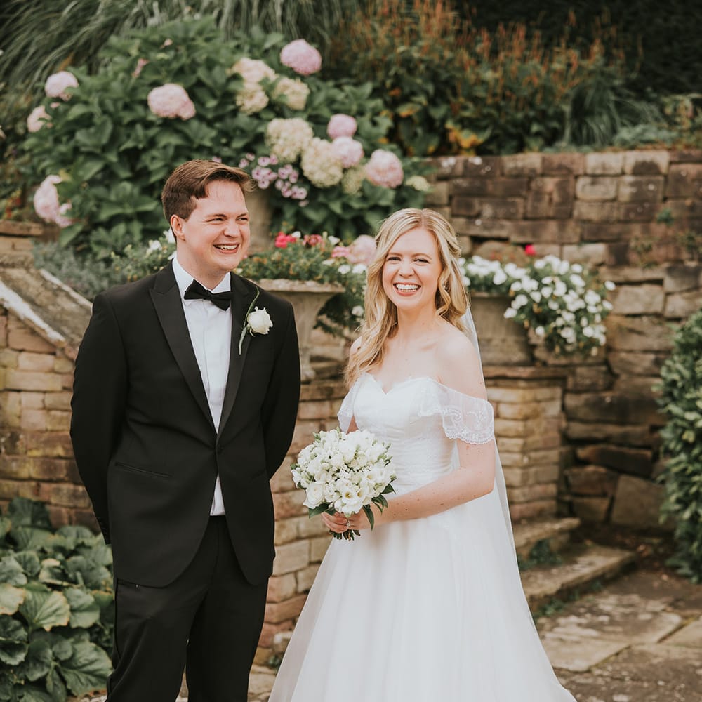 Bride in off the shoulder wedding dress with ballgown skirt with brother in black tie 