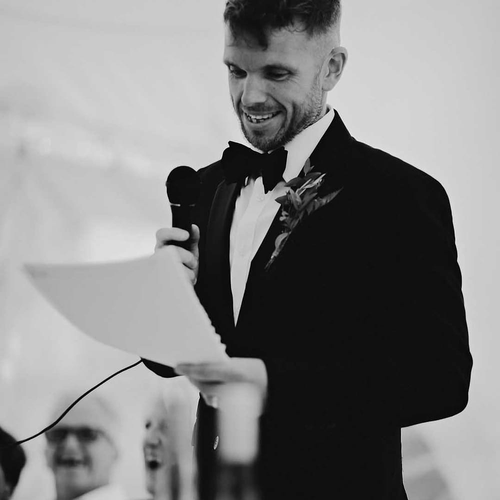 Groom in black tie reads out his wedding speech 