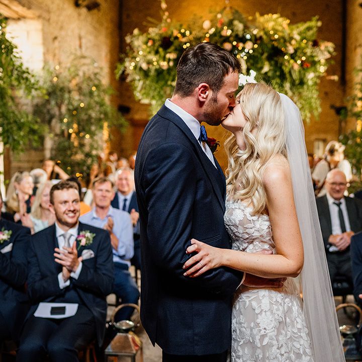 Bride and groom share their first kiss as a married couple at the Cripps Barn wedding venue with greenery 