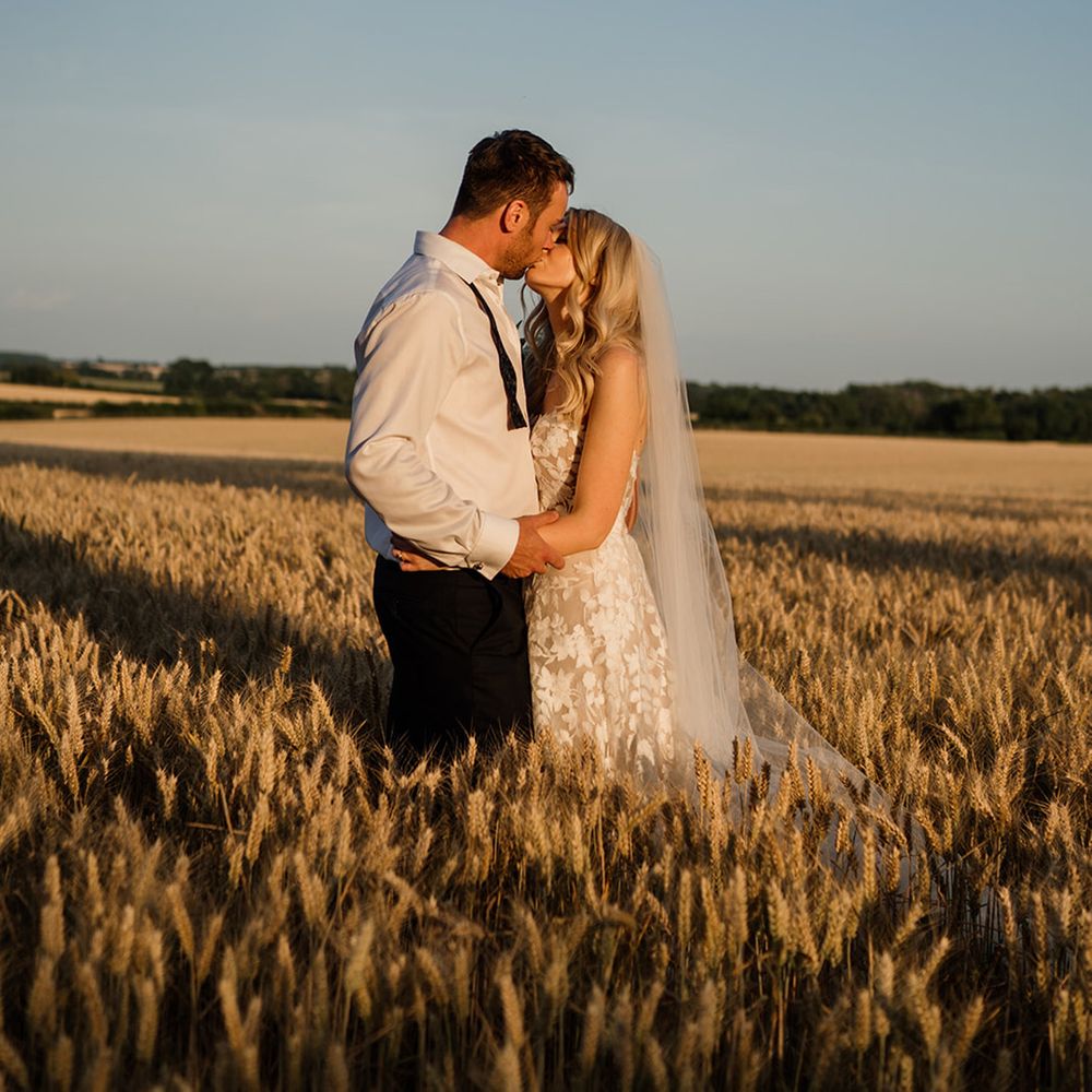 Bride and from share a kiss in a field with bride in Lillian West wedding dress 
