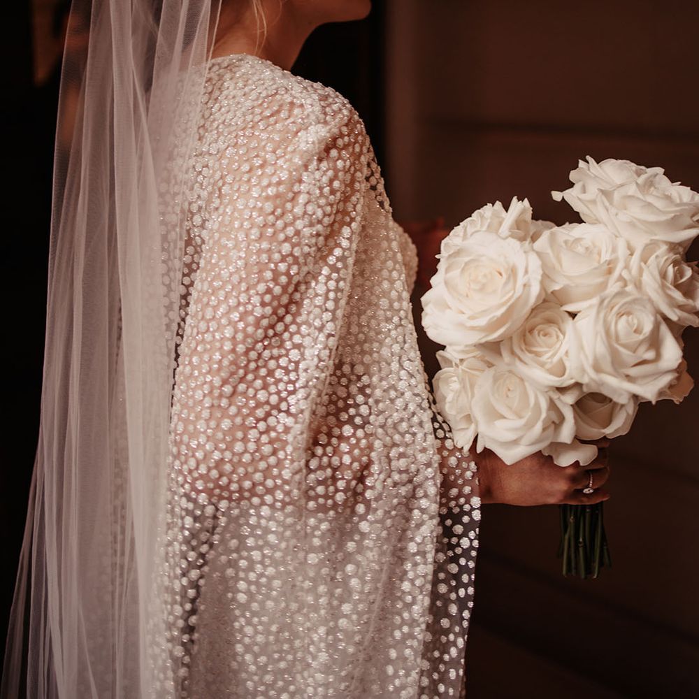 Bride in shimmery Jesus Peiro cape and dress with a white rose wedding bouquet 
