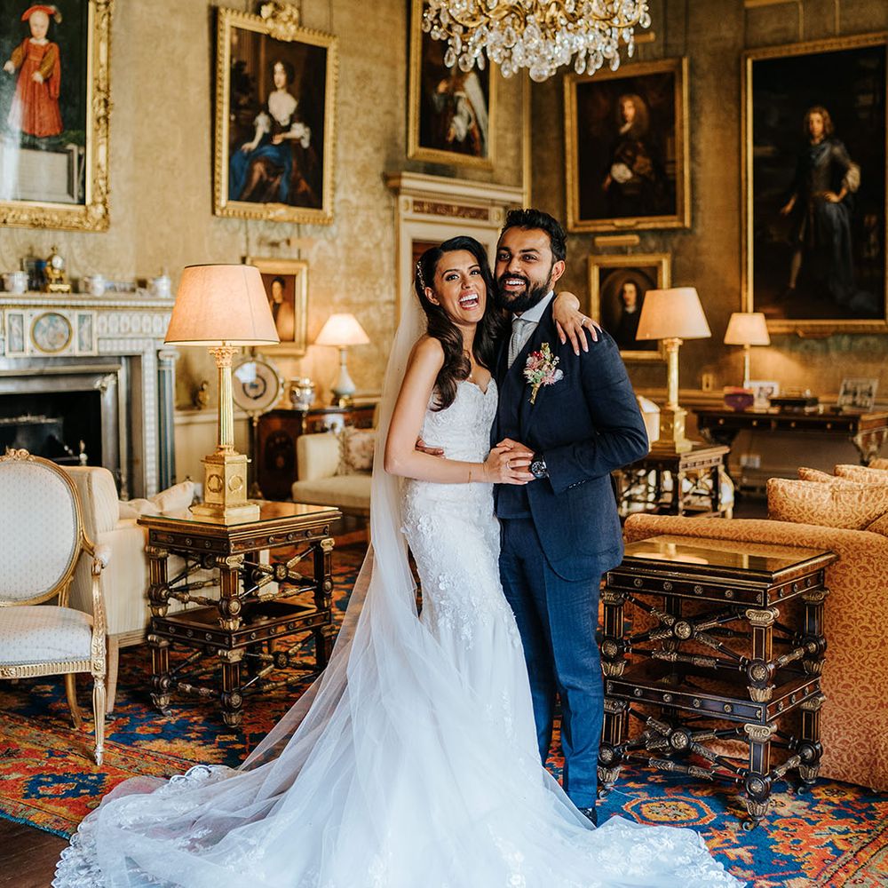 Bride wearing fitted lace wedding dress & groom laugh in grand room at Syon Park 
