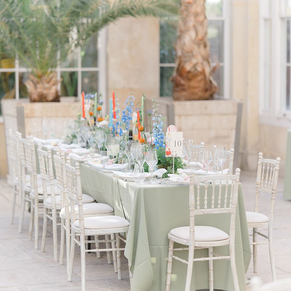 Pastel toned wedding reception at Syon Park with pale green tablecloths, brightly coloured floral arrangements lining the table and white chairs 