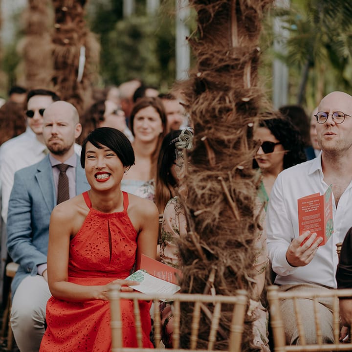 Guest in bright red halter neck dress smiling during ceremony