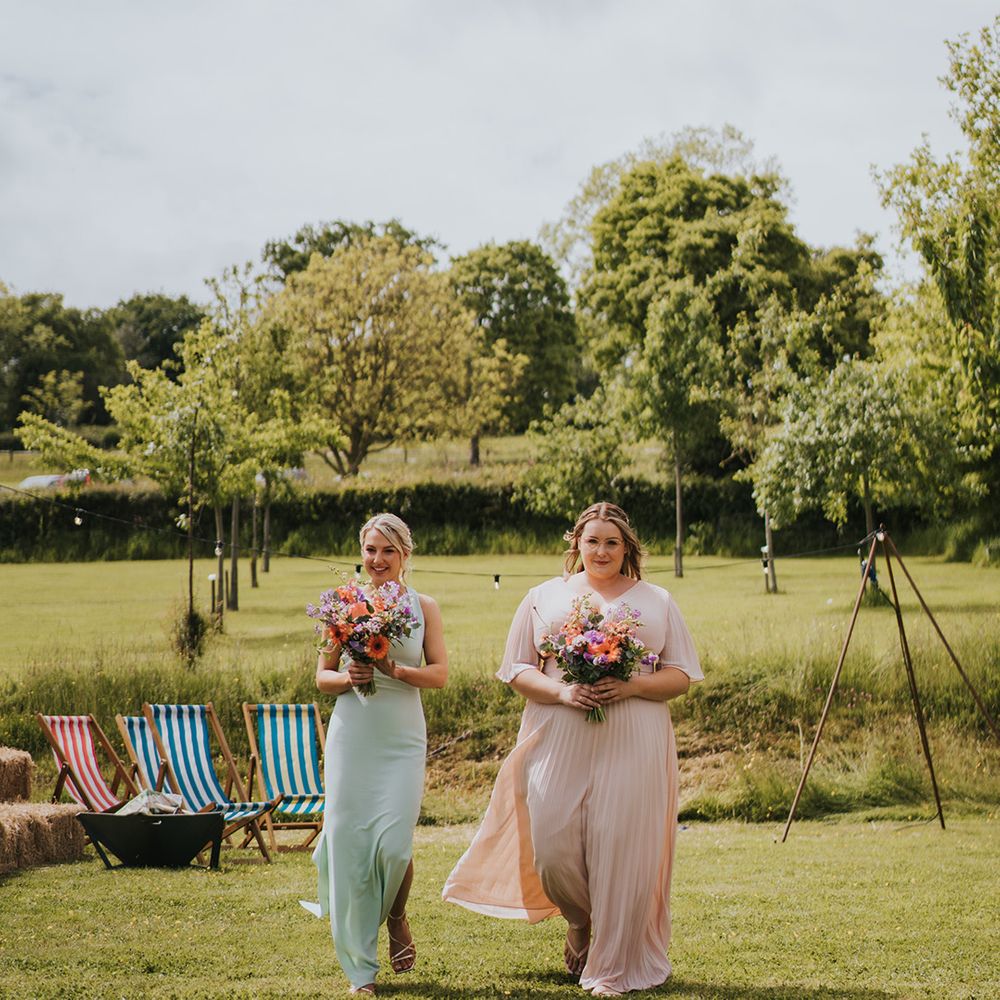 Bridesmaids in mismatched pastel bridesmaid dresses carry colourful floral bouquets 